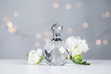 Bir şişe aromatik parfüm ve çiçek, arka plandaki gri ışıklara karşı, yakın plan. Bokeh etkisi