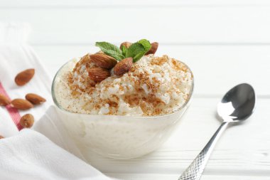 Tarçınlı lezzetli pirinç pudingi, beyaz ahşap masada nane ve badem, yakın plan.