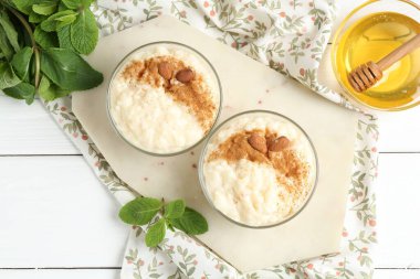 Tarçınlı lezzetli sütlaç, badem, bal ve nane beyaz ahşap masa, düz uzanmış