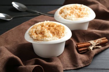 Tarçınlı lezzetli sütlaç ve siyah ahşap masada kaşıklar, yakın plan.