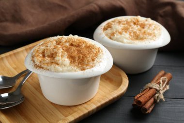 Tarçınlı lezzetli sütlaç ve siyah ahşap masada kaşıklar, yakın plan.