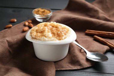 Tarçınlı sütlaç, badem ve kaşık siyah ahşap masada, yakın plan.