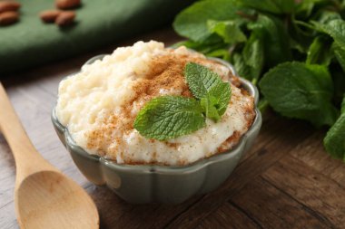 Tarçınlı, naneli, bademli ve ahşap masadaki kaşıklı lezzetli sütlaç.