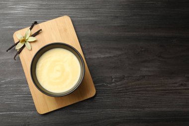 Lezzetli vanilyalı puding kasede, çiçek ve kapsüller ahşap masada, üst manzara. Metin için boşluk