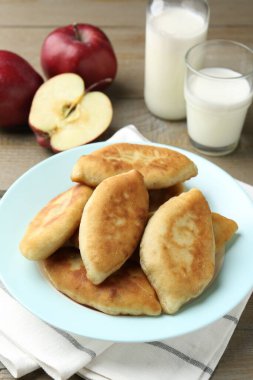 Ahşap masada elmalı ve sütlü lezzetli pirizhki (doldurulmuş turtalar) yakın plan.