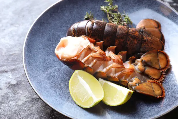 Çiğ ıstakoz kuyruğu, kireç ve kekik karanlık masada, yakın plan.