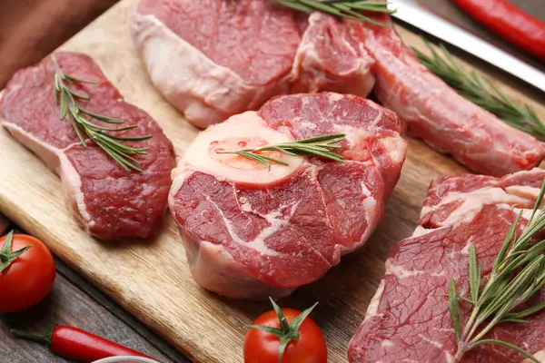 Çiğ et parçaları, biberiye ve domatesler ahşap masada, yakın plan.