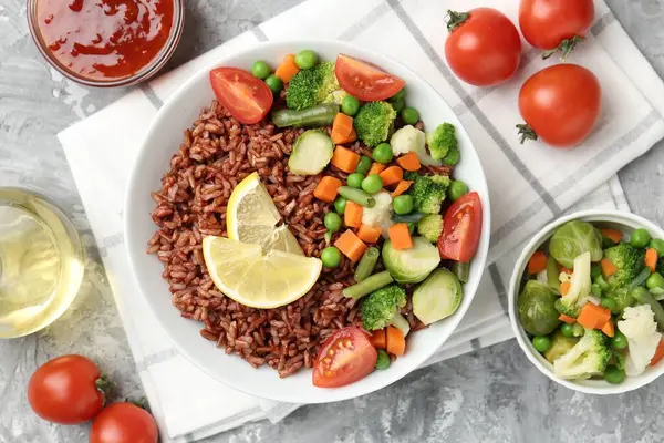 Gri desenli masada servis edilen sebzeli ve limon dilimli lezzetli kahverengi pirinç.