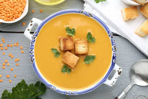 Lezzetli mercimek kremalı çorba. Gri ahşap masada kızarmış ekmeklerle servis ediliyor.