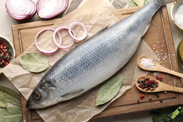 Açık gri masada tuzlanmış ringa balığı ve baharatlar, düz uzanmış.