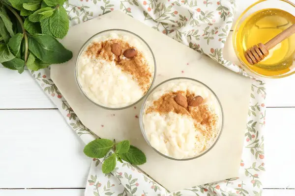 Tarçınlı lezzetli sütlaç, badem, bal ve nane beyaz ahşap masa, düz uzanmış
