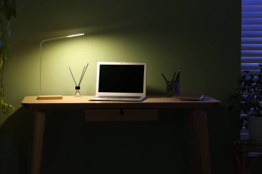 Ev ofisinin ahşap masasında dizüstü bilgisayarı ve lambası olan rahat bir iş yeri.