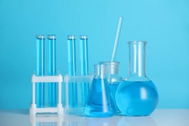 Aynanın yüzeyinde mavi arkaplana karşı sıvı bulunan laboratuvar camları.