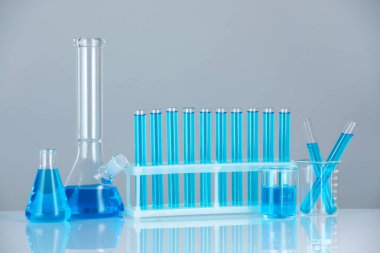 Aynanın yüzeyinde gri arka planda mavi sıvı bulunan laboratuvar camları