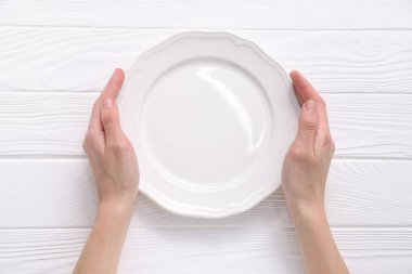 Beyaz ahşap masada boş seramik tabak taşıyan bir kadın.