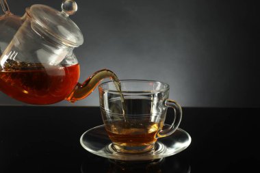Çaydanlıktan taze demlenmiş çayı siyah masaya, cam fincana dökerek.