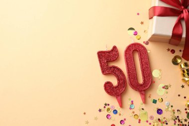 50th birthday. Number shaped candles, gift box and confetti on beige background, flat lay. Space for text
