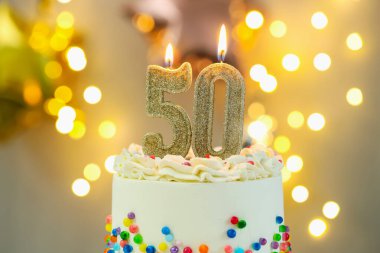 50th birthday. Burning number shaped candles on cake against blurred background with lights, closeup. Bokeh effect