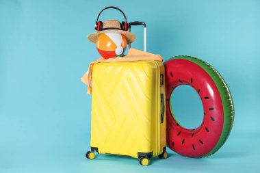 Parlak şişirilebilir yüzük, diğer farklı aksesuarlar, kulaklıklar ve açık mavi arka planda bavul.