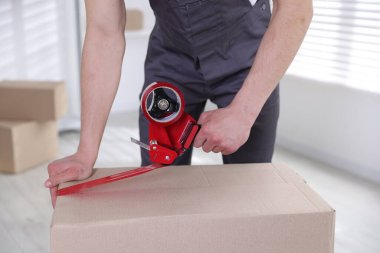 Karton kutuyu kapalı bir yere kapatmak için yapıştırıcılı bant kullanan bir adam.