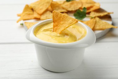 Lezzetli bir peynir sosu ve beyaz ahşap masada nacho cipsi, yakın plan.