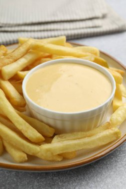 Lezzetli peynir sosu kasede ve patates kızartması gri masada, yakın plan.