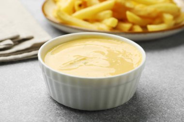 Lezzetli peynir sosu kasede ve patates kızartması gri masada, yakın plan.