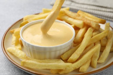 Gri masada patates kızartmasını peynir sosuna batırmak, yakın plan.