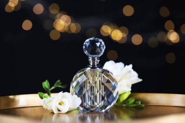 Bir şişe aromatik parfüm ve metal tepside çiçeklerle siyah arka planda bulanık ışıklar, yakın plan. Bokeh etkisi