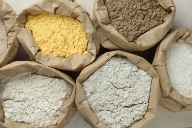 Beyaz masadaki kağıt torbalarda farklı türde un, düz yerde.