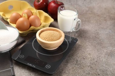 Dijital mutfak terazisi, kahverengi şeker kasesi ve gri masadaki diğer ürünler, yakın plan. Metin için boşluk