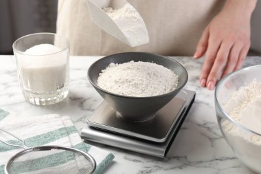 Beyaz mermer masadaki dijital mutfak terazisine şeker koyan kadın, yakın plan.
