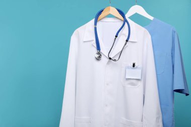 Mavi arka plandaki askılarda steteskop olan sağlık çalışanları üniformaları.