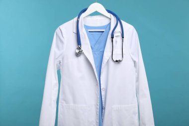 Mavi arka planda asılı steteskoplu doktor ceketi.
