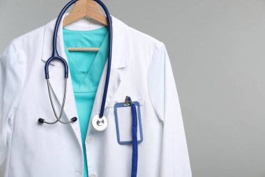 Üzerinde steteskop ve rozet olan doktor ceketi gri arka planda.