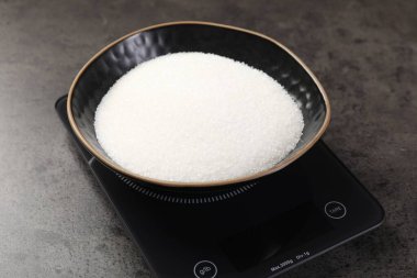 Dijital mutfak terazisi, gri masada bir kase şeker, yakın plan.