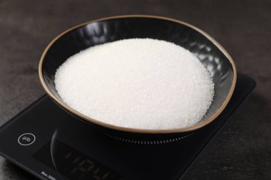 Dijital mutfak terazisi, gri masada bir kase şeker, yakın plan.