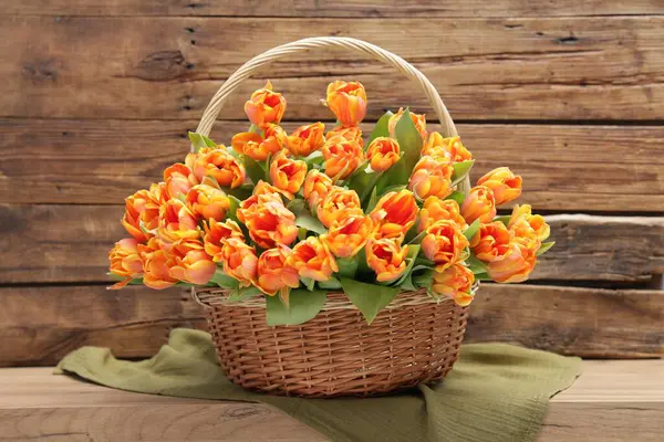 Hasır sepetteki güzel laleler ahşap masada.