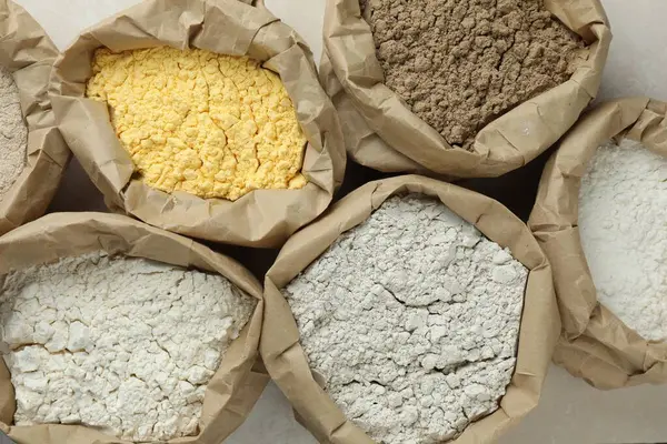 Beyaz masadaki kağıt torbalarda farklı türde un, düz yerde.