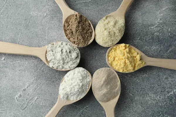 Gri masadaki kaşıklarda farklı türde un, düz.