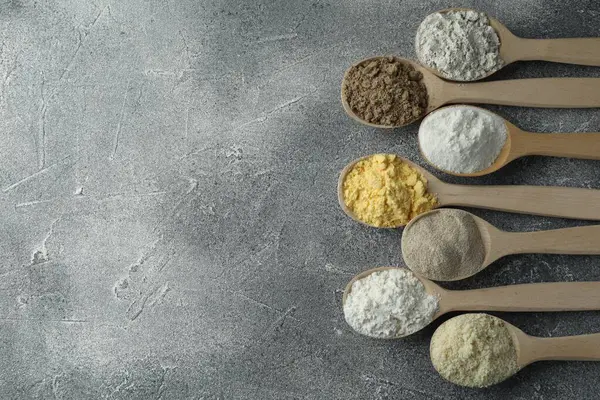 Gri masadaki kaşıklarda farklı türde un, düz. Metin için boşluk