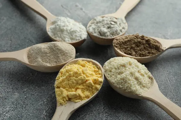 Gri masadaki kaşıklarda farklı türde un, yakın plan.