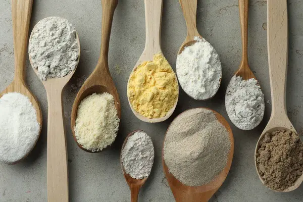 Açık gri masadaki kaşıklarda farklı türde un, düz.