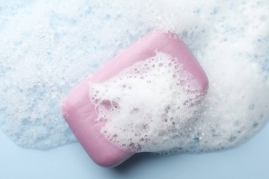 Açık mavi arkaplanda köpük olan sabun çubuğu, üst görünüm