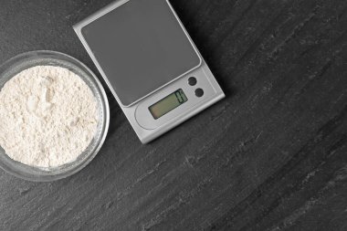 Elektronik mutfak terazisi ve koyu dokulu masa üzerinde un bulunan bir kase, düz. Metin için boşluk