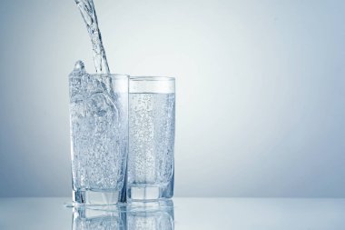 Açık gri arka planda bardaklara ferahlatıcı soda dökülüyor, yakın plan. Metin için boşluk