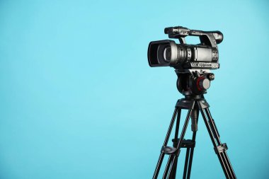 Açık mavi arkaplanda tripodu olan modern video kamera, metin için boşluk
