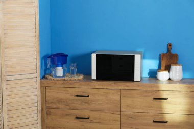 Closed microwave oven and kitchen utensils on wooden cabinet indoors