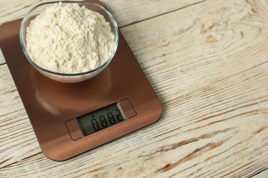 Modern electronic kitchen scale with bowl of flour on wooden table, closeup. Space for text