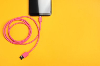 USB kablosu turuncu arka plandaki akıllı telefona bağlı. Metin için boşluk